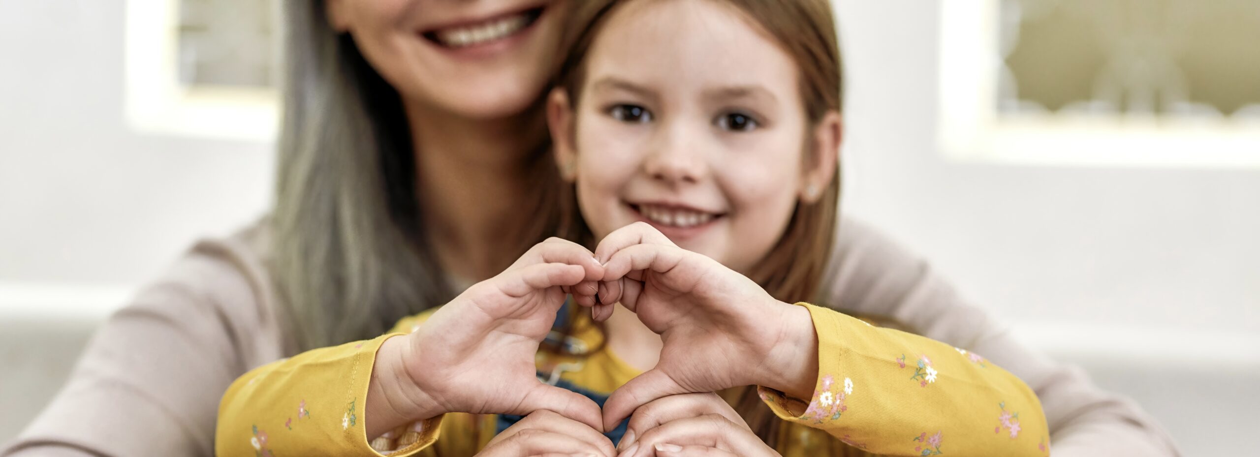 Spreading love. Close up portrait of little girl granddaughter spending time together with her loving granny. They are smiling and showing heart sign. Front view. Selective focus on hands