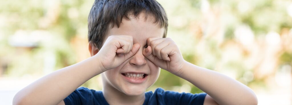 Child suffering itching scratching eyes outdoors in a park