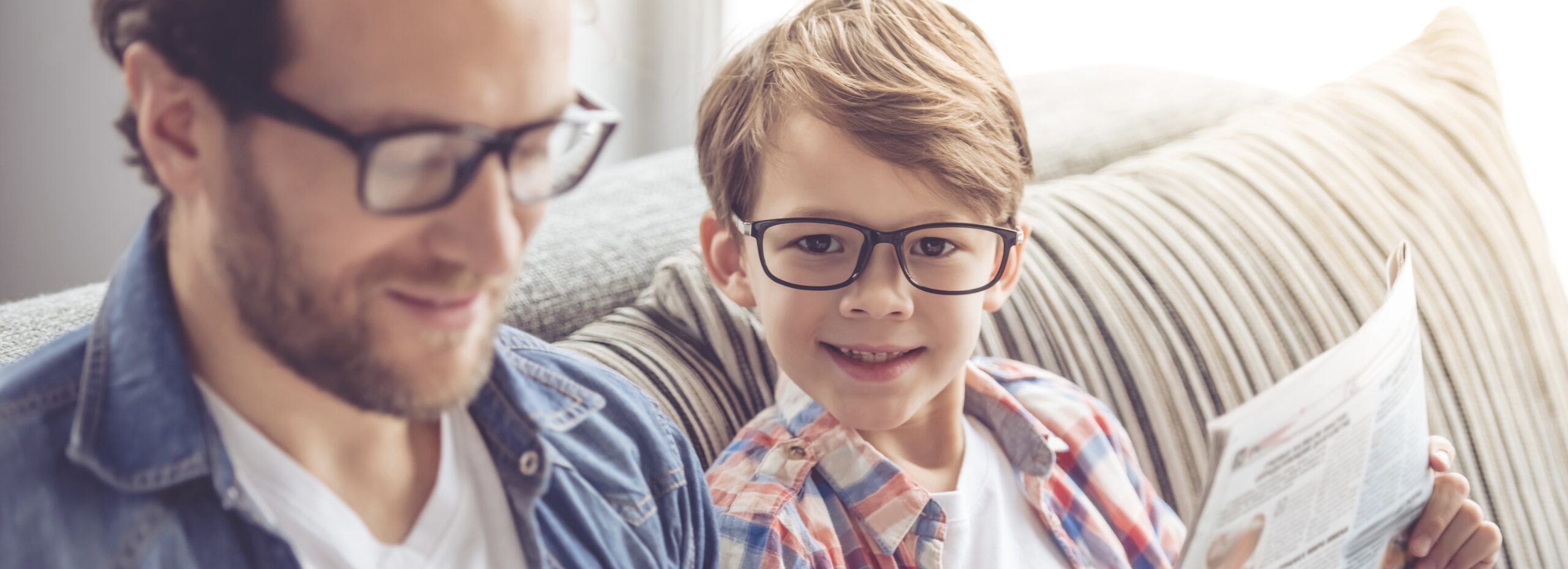 Father and son are reading newspapers and smiling while spending time together at home