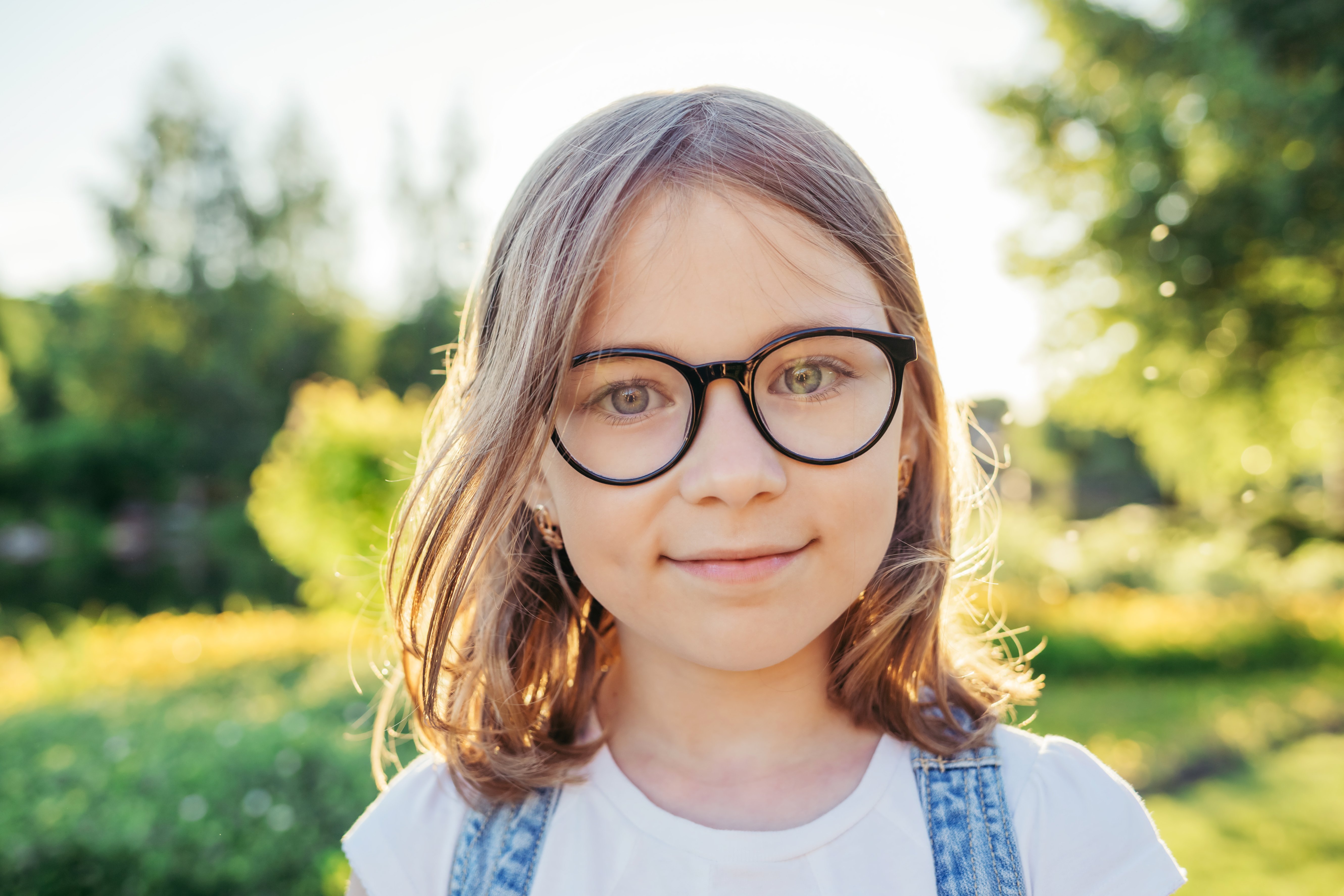 Girl looking at camera and smiling in nature. Summer leisure. Girl in glasses with black rim.