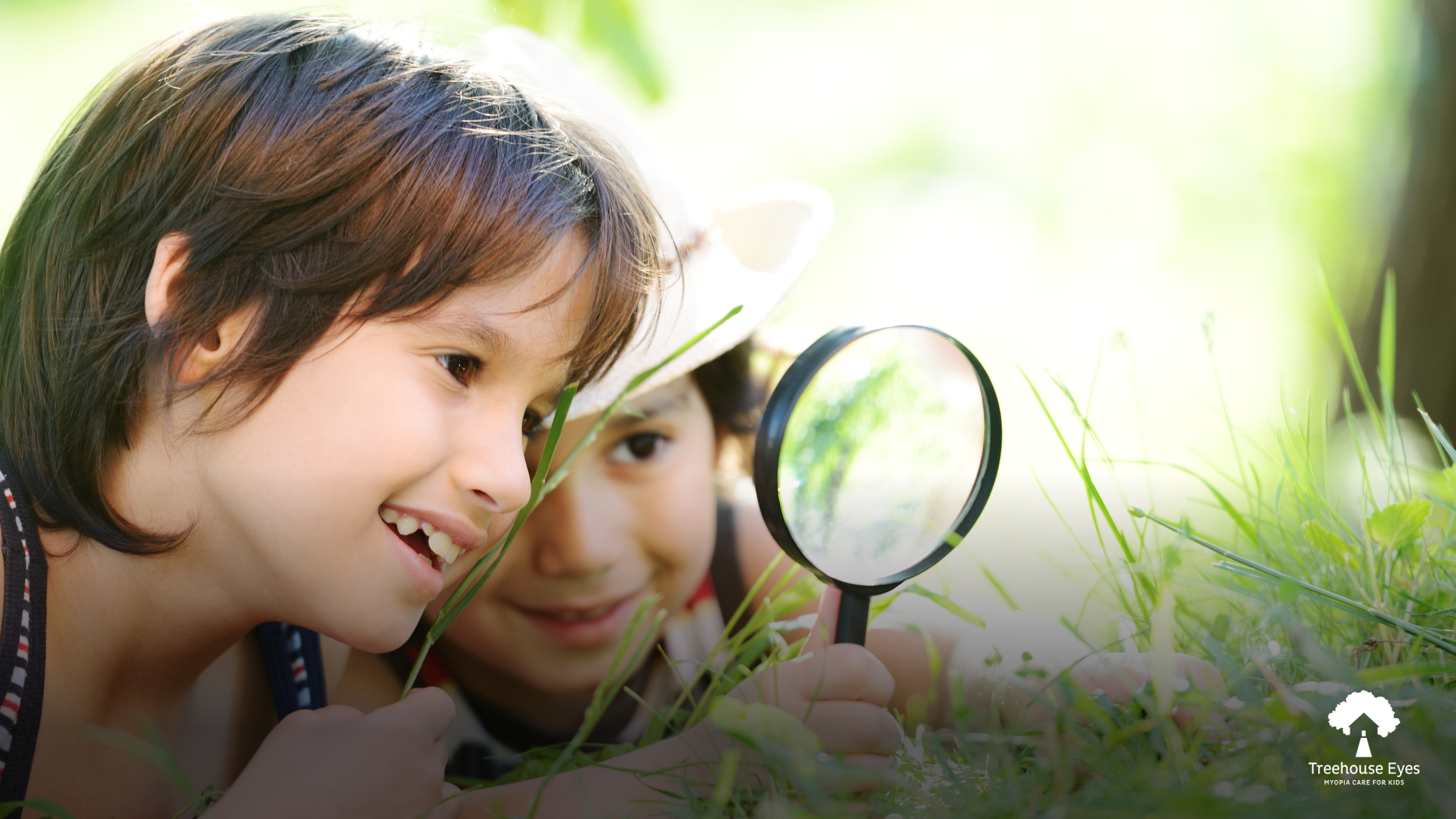 Two kids looking through a magnifying glass at the grass outside.