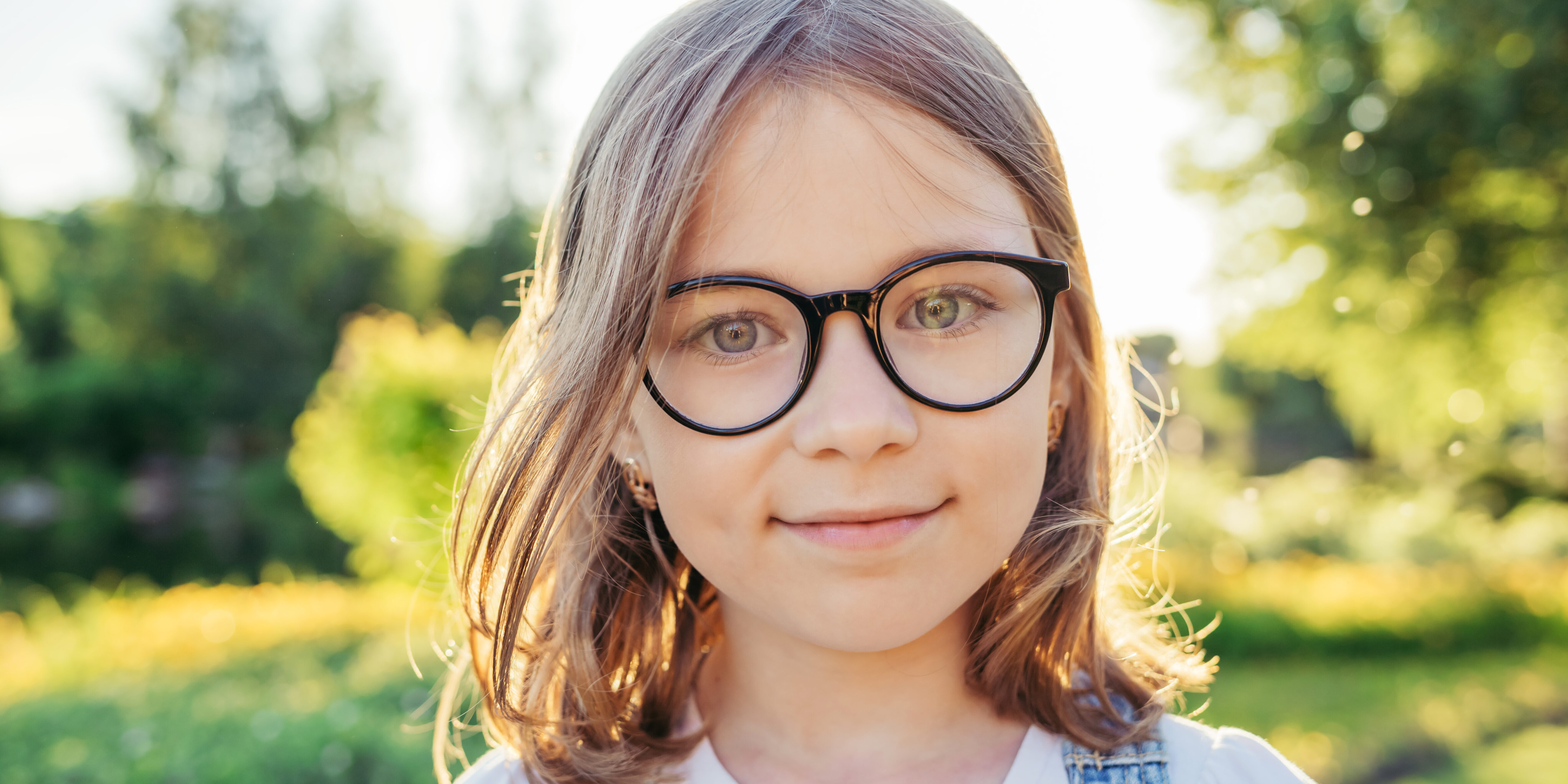 Girl looking at camera and smiling in nature. Summer leisure. Girl in glasses with black rim.